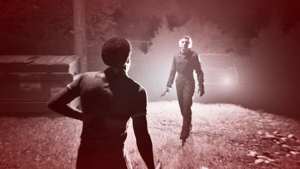 Screenshot from Halloween: The Game showing a tense standoff, with one character approaching another in a dimly lit outdoor area.