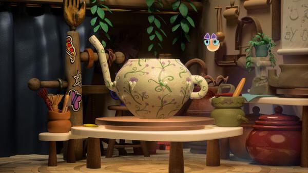 Screenshot from Kiln showing a detailed teapot with floral patterns on a pottery wheel in a cozy, decorated workshop.