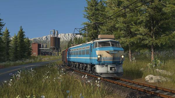 Transport Fever 3 screenshot showing a blue train traveling on tracks through a scenic forested area with mountains in the background.