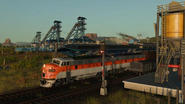 A Transport Fever 3 screenshot showing a red and white train passing a rural station near industrial buildings and mining equipment.
