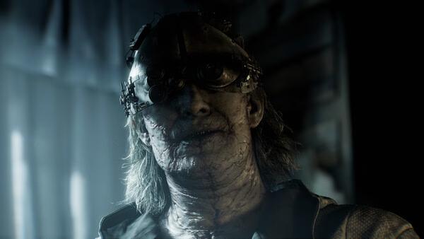 A screenshot from Resident Evil Requiem shows a sinister character with mechanical enhancements in a dimly lit environment.