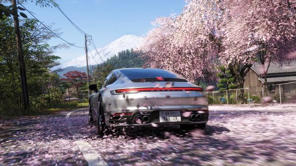 Forza Horizon 6 screenshot: A sleek car speeds through a scenic road lined with cherry blossoms, petals swirling in the air.