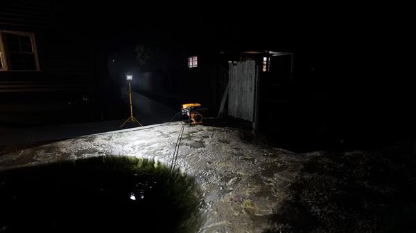 Screenshot from DrainSim showing a night scene with floodlights illuminating a muddy area and a small shed.