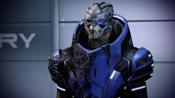 Mass Effect™ Legendary Edition screenshot: A character in blue armor stands against a gray wall, displaying a futuristic design.