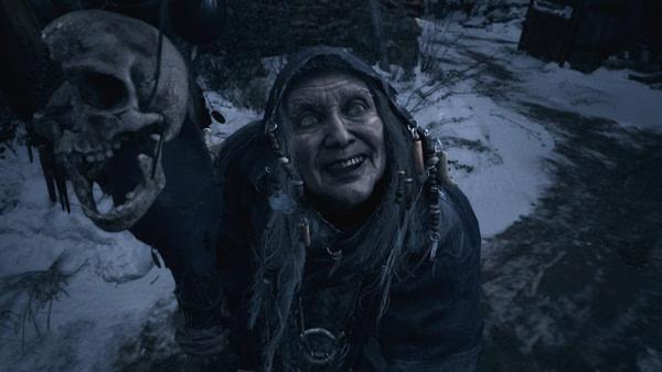 Resident Evil Village screenshot: A mysterious figure in dark clothing holds a staff topped with a skull in a snowy environment.