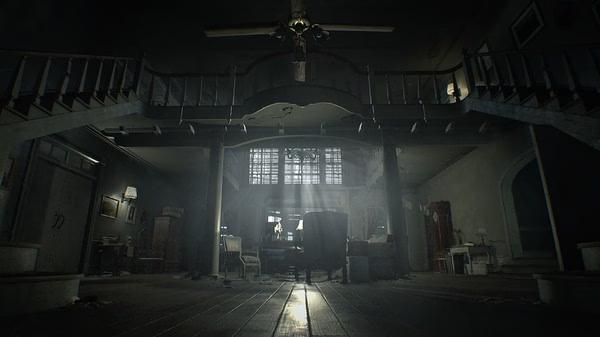 Screenshot from Resident Evil 7 Biohazard showing an eerie, dimly lit mansion interior with a grand staircase and scattered furniture.