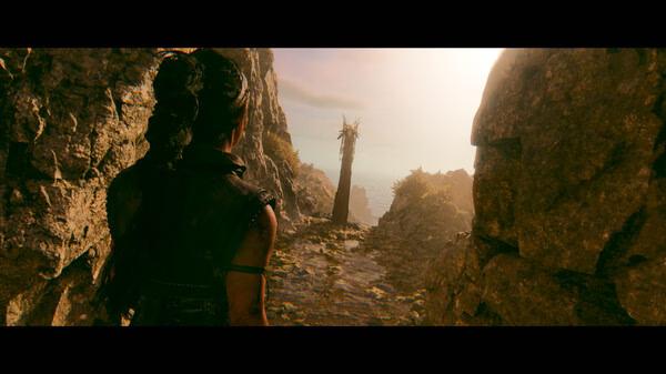 Screenshot from Hellblade II: Senua’s Saga showing Senua walking through a rocky path towards a distant, sunlit landscape.