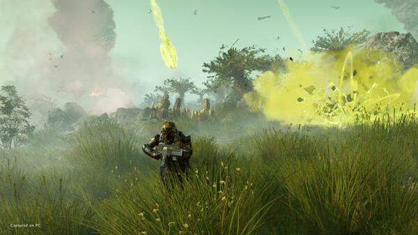 HELLDIVERS 2 screenshot: A heavily armored soldier stands in tall grass, aiming a weapon, with an explosion and aliens in the background.