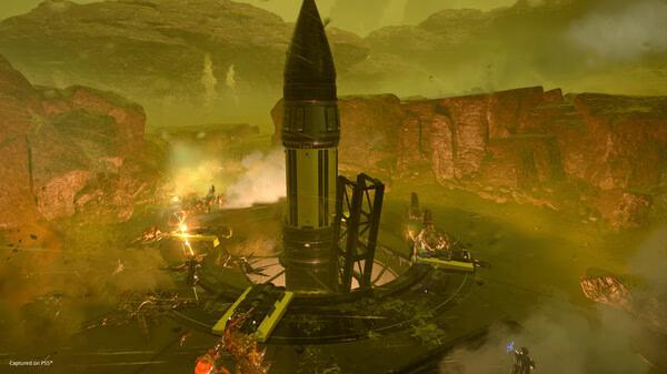 HELLDIVERS 2 screenshot showing a group of players battling alien creatures around a large rocket in a rocky, green-tinted landscape.