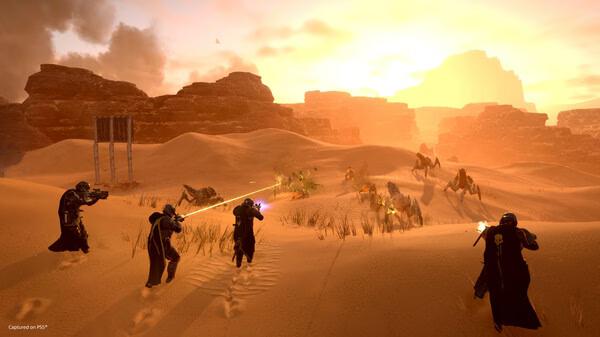 Screenshot of HELLDIVERS 2: Four players in dark armor engage spider-like aliens in a vast, sunlit desert landscape.