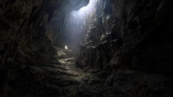 Fatekeeper screenshot: A dimly lit cavern with rugged walls and a beam of light illuminating the entrance.