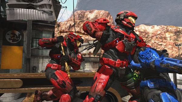 Red and blue armored Spartans engage in combat in a Halo: The Master Chief Collection screenshot set in a rugged outdoor environment.