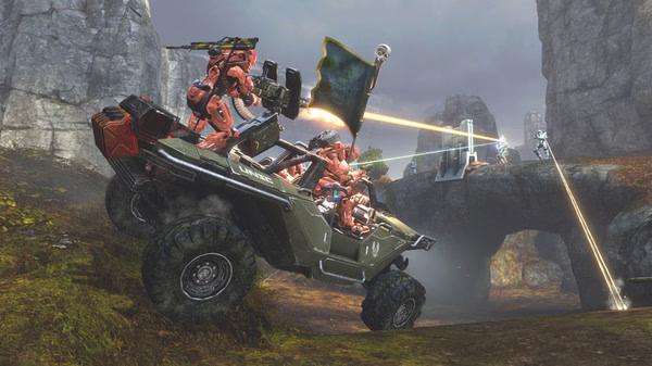 Screenshot from Halo: The Master Chief Collection showing armored soldiers driving a vehicle while engaged in a laser battle on rocky terrain.