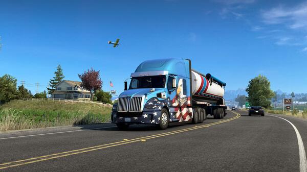 Screenshot of American Truck Simulator showing a truck with a patriotic design on a highway, with a plane in the sky.