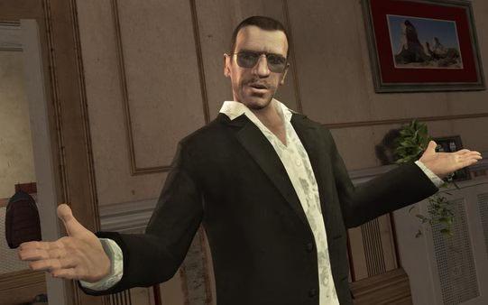 A Grand Theft Auto IV screenshot showing a man in a black suit with arms outstretched, standing in a room with wall decor and furniture.