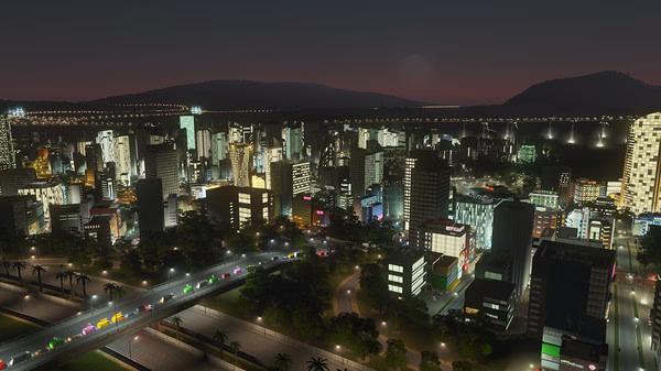 A Cities: Skylines screenshot showcasing a vibrant cityscape at night, with lit-up skyscrapers, roads, and bridges.