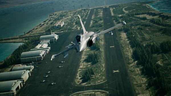 A jet flies over a military airbase runway surrounded by trees in this ACE COMBAT 7: SKIES UNKNOWN screenshot.
