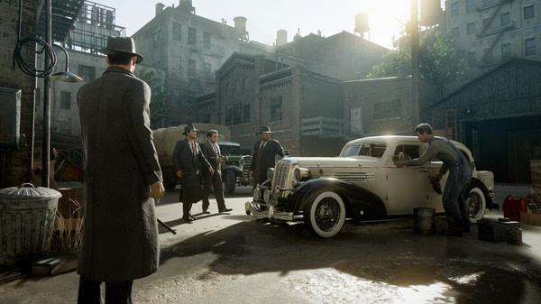Screenshot from Mafia: Definitive Edition showing men in suits and hats near a vintage car in a sunlit alley.