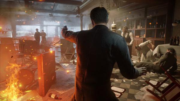 Screenshot from Mafia: Definitive Edition showing a man in a suit aiming a gun in a chaotic, fiery bar scene.