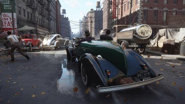Screenshot from Mafia: Definitive Edition showing a vintage green car driving through a bustling city street with various other vehicles.