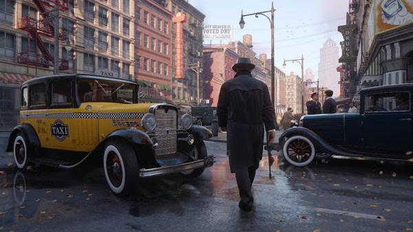 Screenshot from Mafia: Definitive Edition showing a man in a trench coat walking past vintage cars on a city street.
