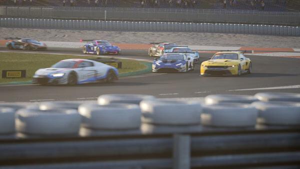 A screenshot from Assetto Corsa Competizione showing racing cars competing on a track with tire barriers in the foreground.