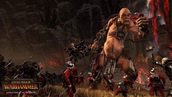 Total War: WARHAMMER screenshot: A giant creature towers over an army of soldiers in red uniforms amidst a fiery battlefield.