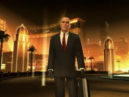 Hitman: Blood Money screenshot of a bald man in a suit holding a briefcase in front of a lit up building at night.