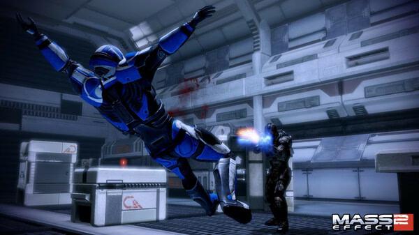 A Mass Effect 2 screenshot showing a soldier in blue armor mid-air as another character fires a weapon inside a futuristic facility.