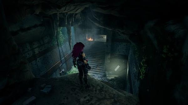 Darksiders III screenshot: A character with red hair stands poised in a dimly lit cave tunnel, surrounded by stone and vegetation.
