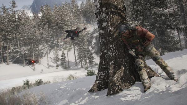 A screenshot from Tom Clancy's Ghost Recon Breakpoint shows a soldier hiding behind a snowy tree as drones patrol the forest.