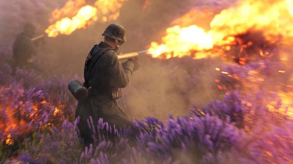 Battlefield V screenshot: A soldier in uniform fires a flamethrower amidst purple flowers, with intense flames illuminating the scene.