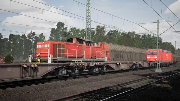 Train Sim World 6 screenshot: Two red diesel locomotives pulling freight cars on tracks surrounded by trees and power lines.
