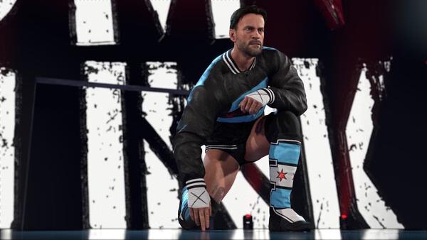 Screenshot from WWE 2K26 showing a wrestler in a black jacket and blue boots, kneeling in front of a large graphic background.