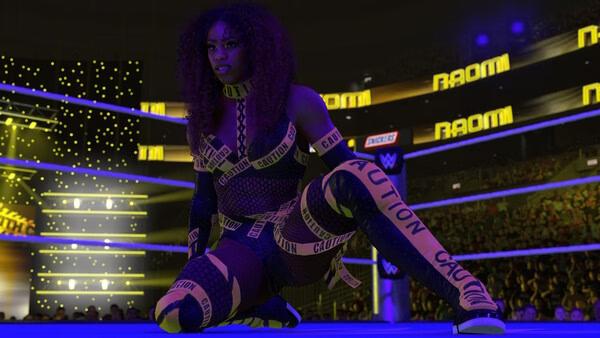 A WWE 2K26 screenshot showing a wrestler kneeling in the ring, wearing a caution-tape-themed outfit under bright arena lights.
