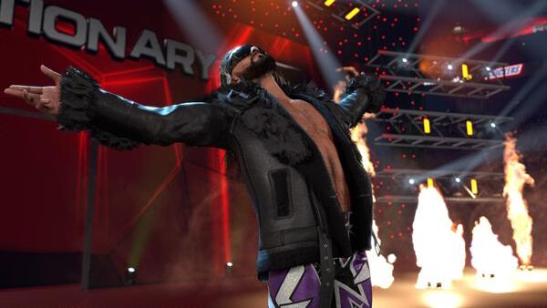 Screenshot from WWE 2K26 showing a wrestler in a black jacket, arms spread wide, surrounded by flames and stage lights.
