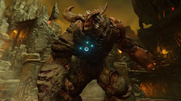A DOOM screenshot showing a towering demon with glowing blue symbols on its chest in a fiery, desolate environment.
