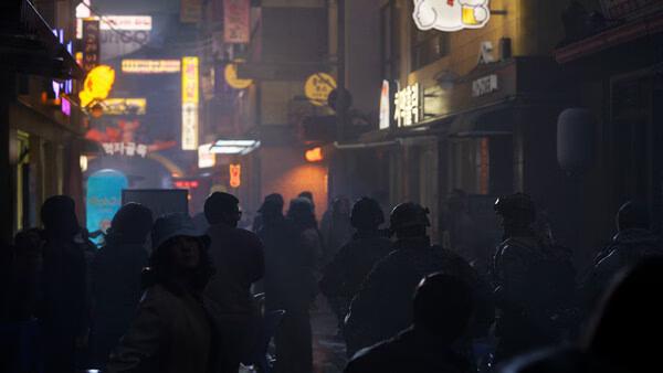 A screenshot from Call of Duty®: Modern Warfare® 4 showing soldiers and civilians in a neon-lit urban alley at night.