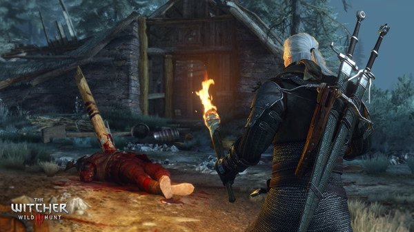 Geralt holds a torch near a cabin and a fallen figure in a forest in this screenshot from The Witcher 3: Wild Hunt.