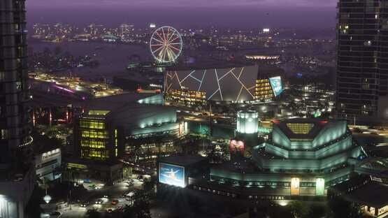 A screenshot from Grand Theft Auto VI (PlayStation 5) shows a vibrant cityscape at night with a lit Ferris wheel and modern buildings.