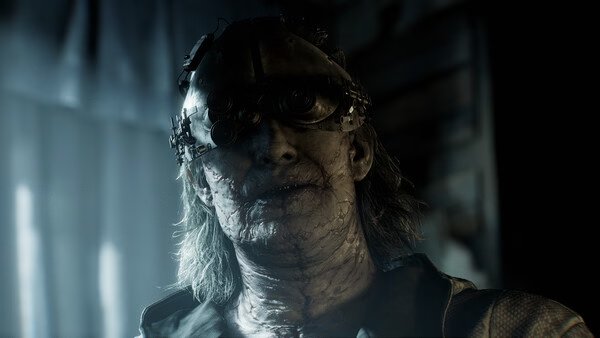 A screenshot from Resident Evil Requiem shows a sinister character with mechanical enhancements in a dimly lit environment.