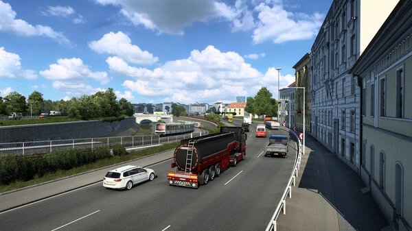 Screenshot of Euro Truck Simulator 2 showing a tanker truck driving on a busy city road with cars, buildings, and a bridge in the background.