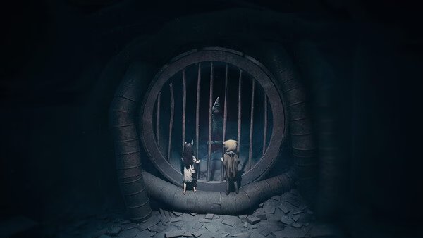 Screenshot from REANIMAL: Two characters stand in front of a large, circular barred gate in a dimly lit, mysterious setting.