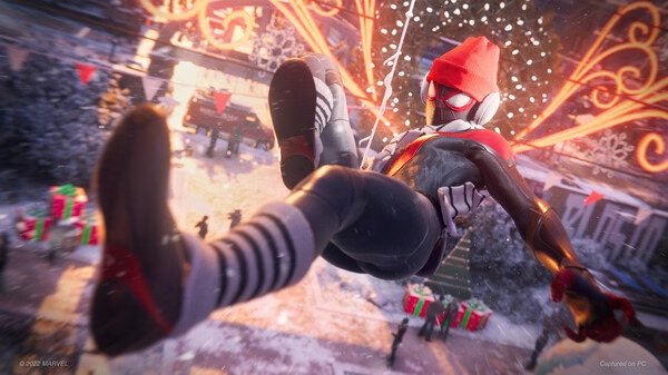 Screenshot of Marvel’s Spider-Man: Miles Morales featuring Miles swinging through a festive, snowy cityscape with holiday decorations.