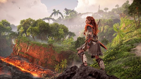 A screenshot from Horizon Forbidden West™ Complete Edition shows Aloy standing on a rocky cliff overlooking a lush, volcanic landscape.