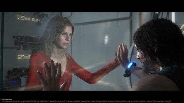 Screenshot from DEATH STRANDING DIRECTOR'S CUT shows two characters touching hands across a glass partition in a futuristic setting.