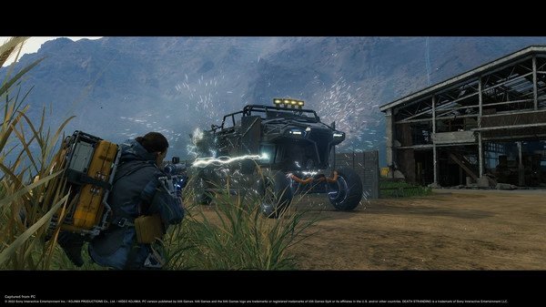 Screenshot from DEATH STRANDING DIRECTOR'S CUT showing a character with a backpack aiming an electric weapon at a vehicle in a rugged landscape.