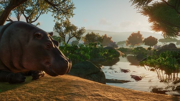 A screenshot from Planet Zoo showing a hippo resting by a lush, tranquil riverbank with trees and hills in the background.