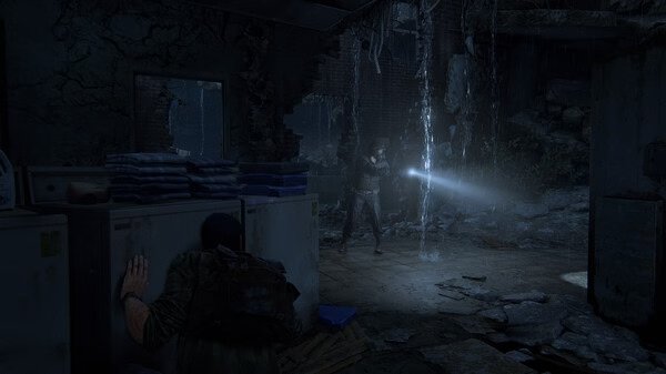 A dimly lit room in 'The Last of Us Part I' screenshot shows a character hiding from an enemy with a flashlight.