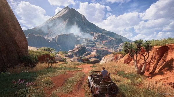 Screenshot from UNCHARTED: Legacy of Thieves Collection showing a jeep driving towards a distant mountain under a cloudy sky.